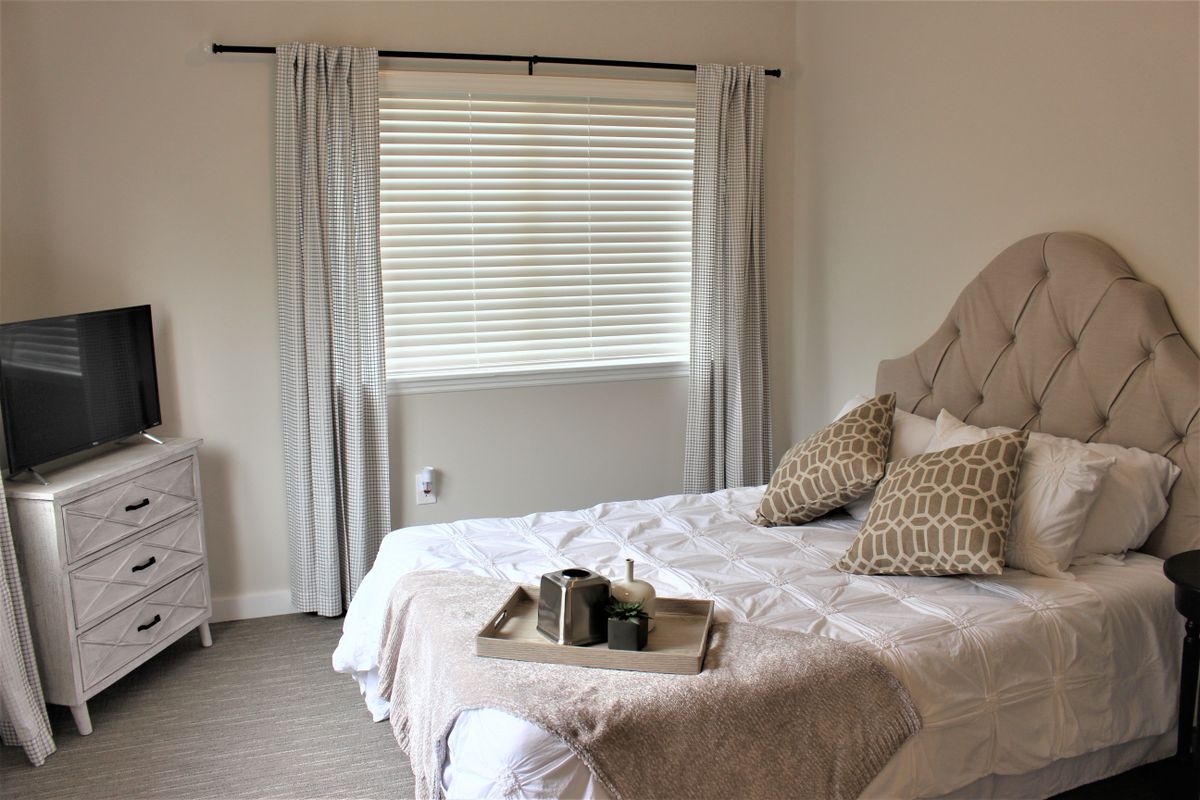 A cozy bedroom with a neatly arranged bed, featuring a decorative tray and neutral color tones.