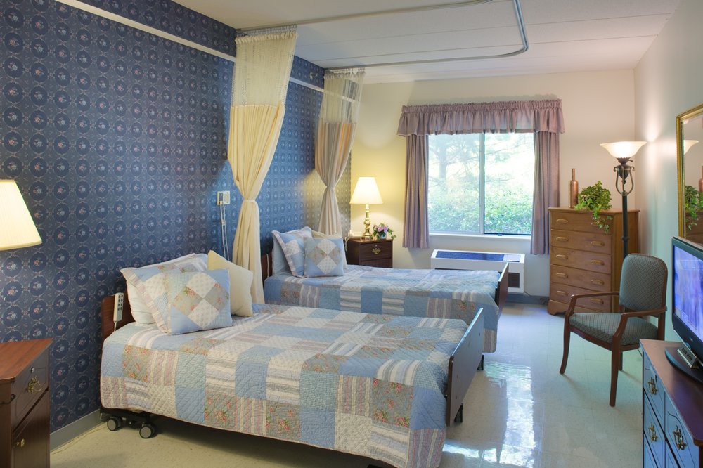 A cozy hospital room with two twin beds, decorated in soft colors and featuring a large window.
