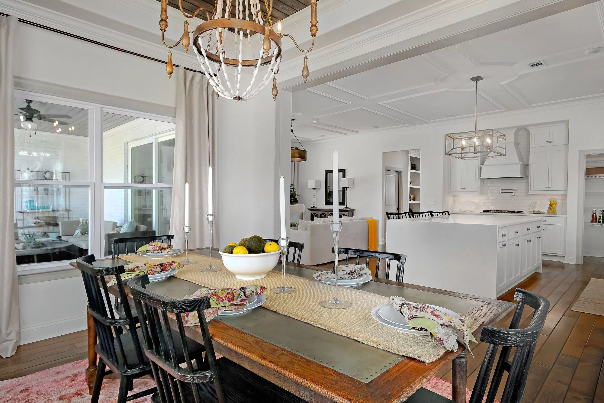 A modern dining area with a view into the kitchen, featuring elegant table settings and a chandelier.