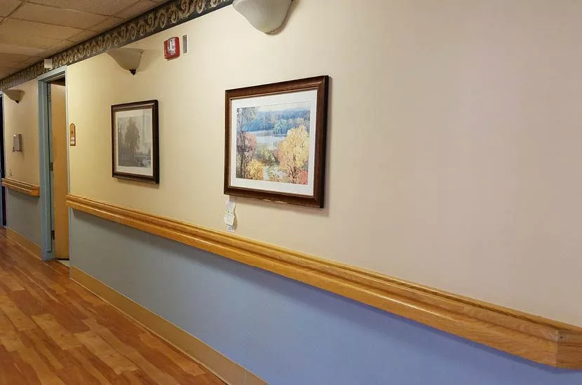 A hallway with framed paintings and a wooden handrail on the wall.