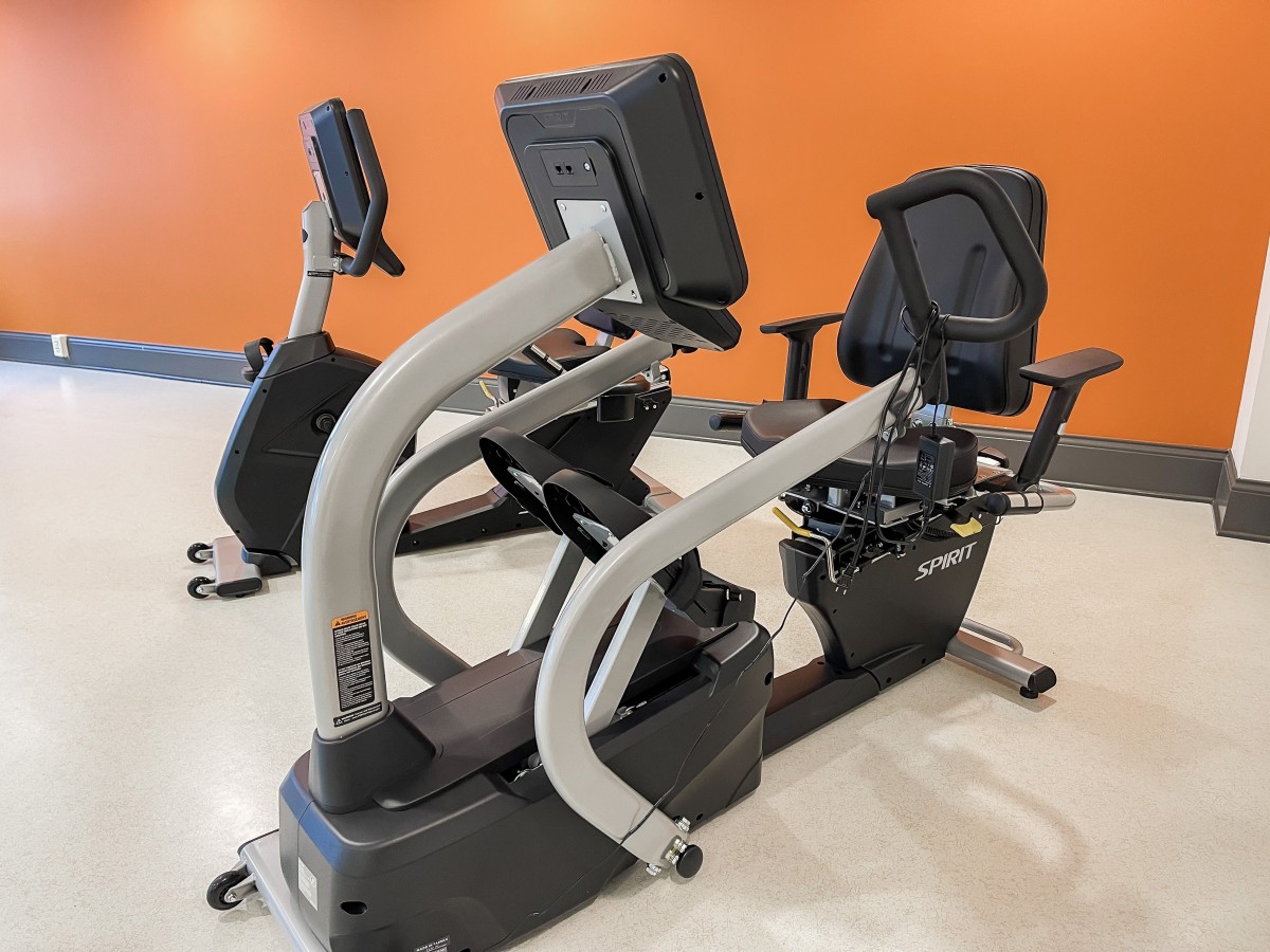 A pair of recumbent exercise bikes in a gym setting with an orange wall.
