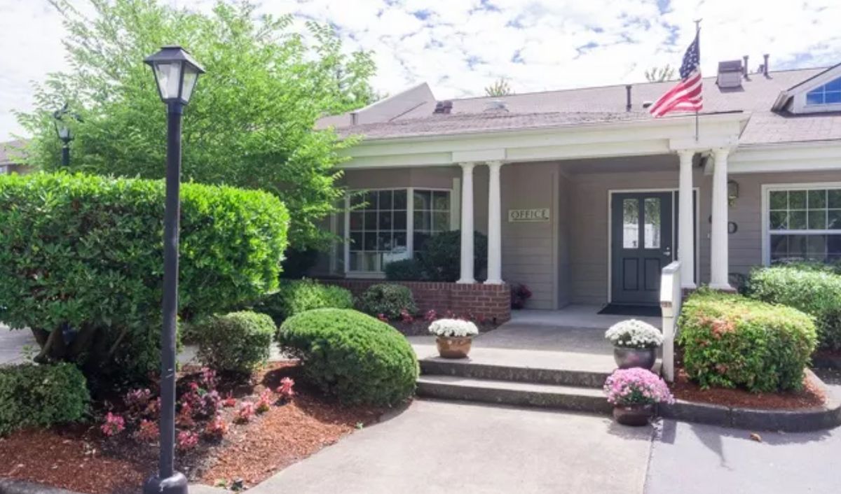 A well-maintained house with a front porch, surrounded by neatly landscaped gardens and trees.