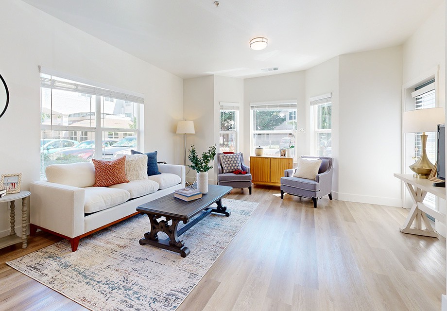 A bright and modern living room with a sofa, chairs, and a coffee table, accented by large windows allowing natural light.