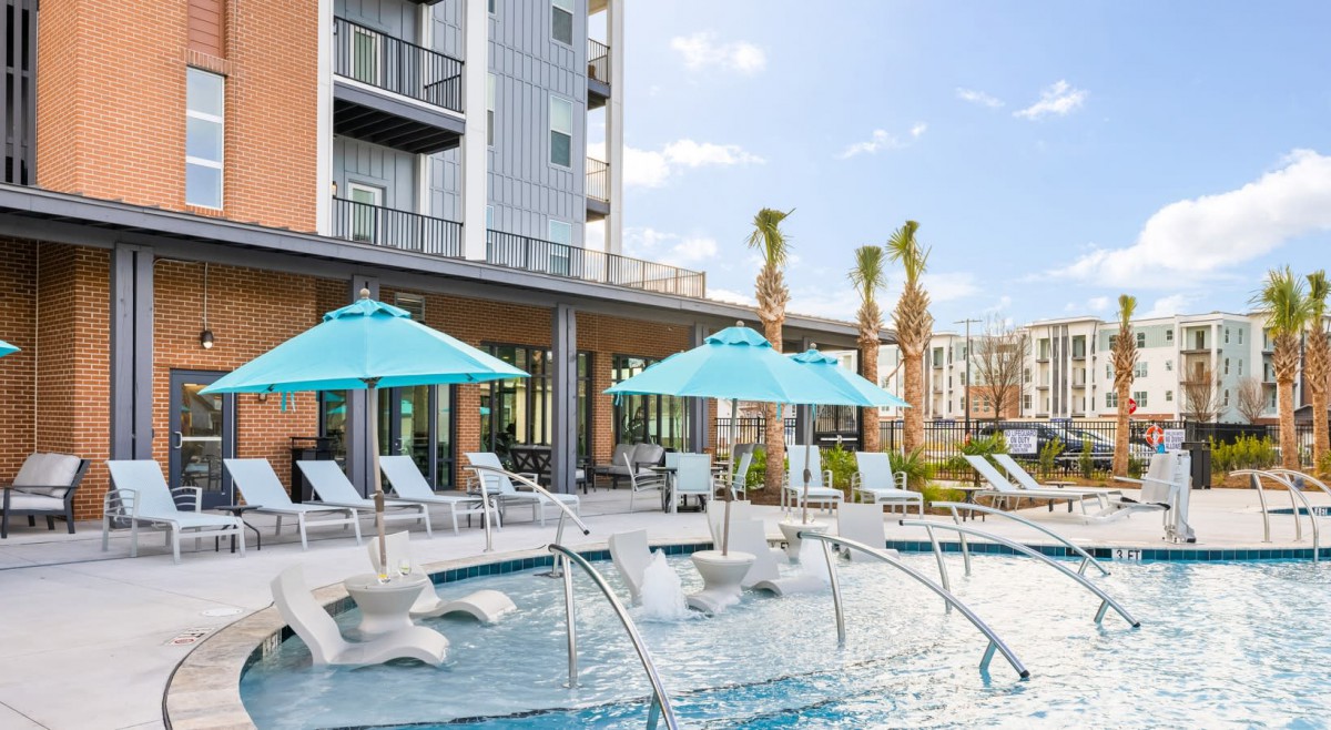 A modern outdoor pool area at a hotel, featuring lounge chairs and umbrellas amidst palm trees.