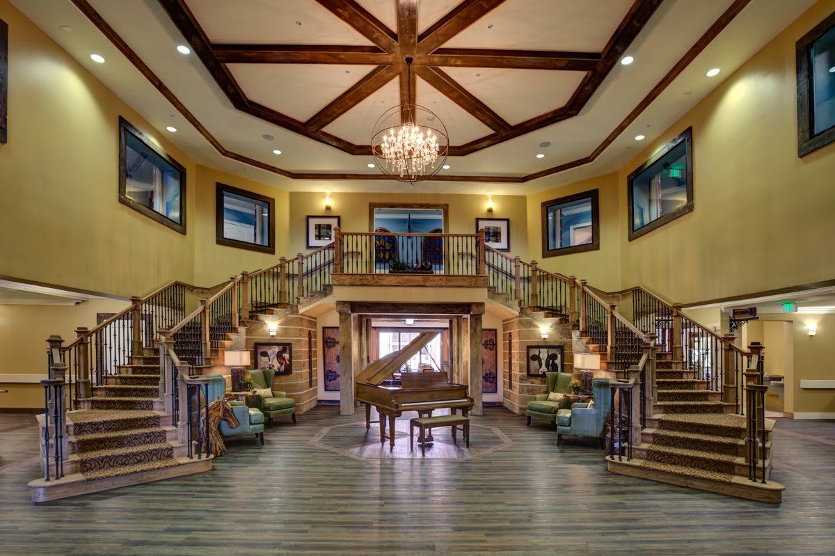 A luxurious grand foyer with a sweeping staircase and elegant chandelier, centered around a grand piano.