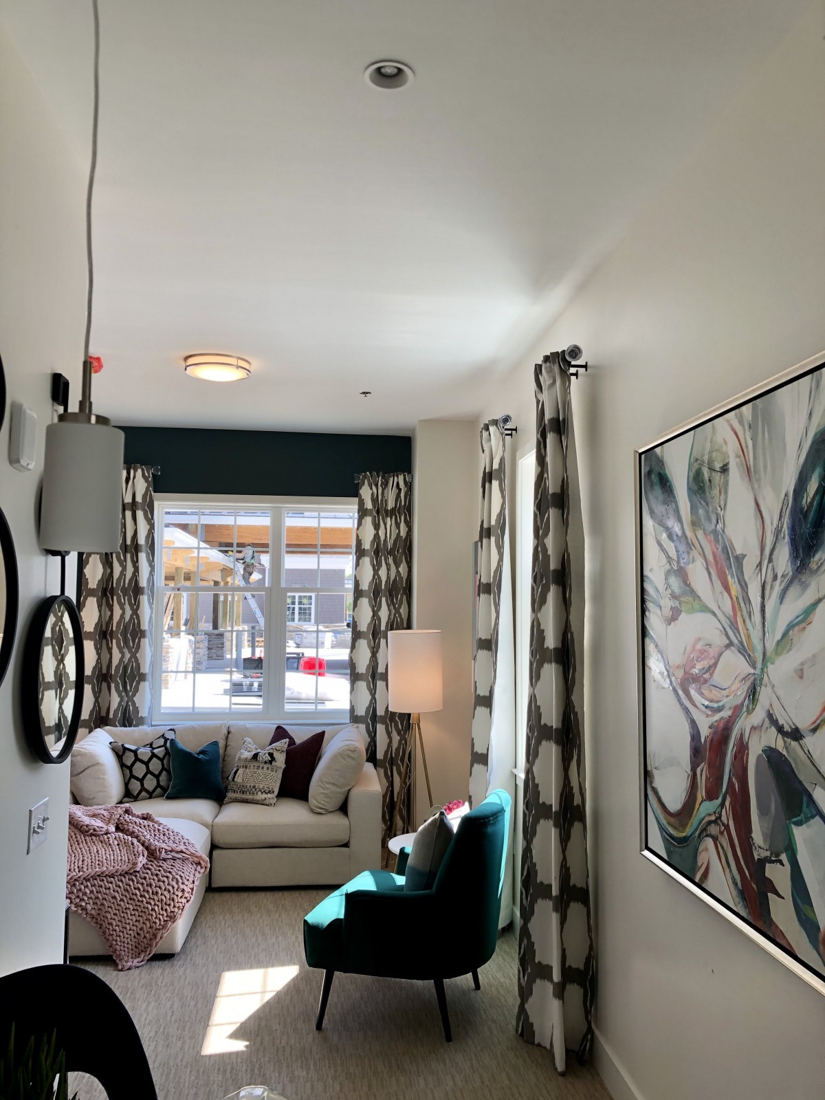 A cozy living room with stylish decor, featuring a comfortable sofa, large window with patterned curtains, modern wall art, and ambient lighting.