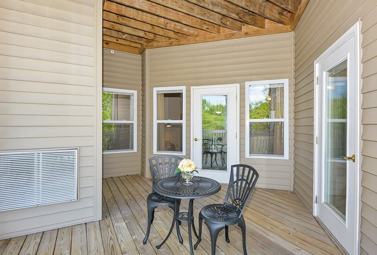 A cozy patio with a small black table and two chairs, featuring a decorative vase with flowers on a wooden deck.