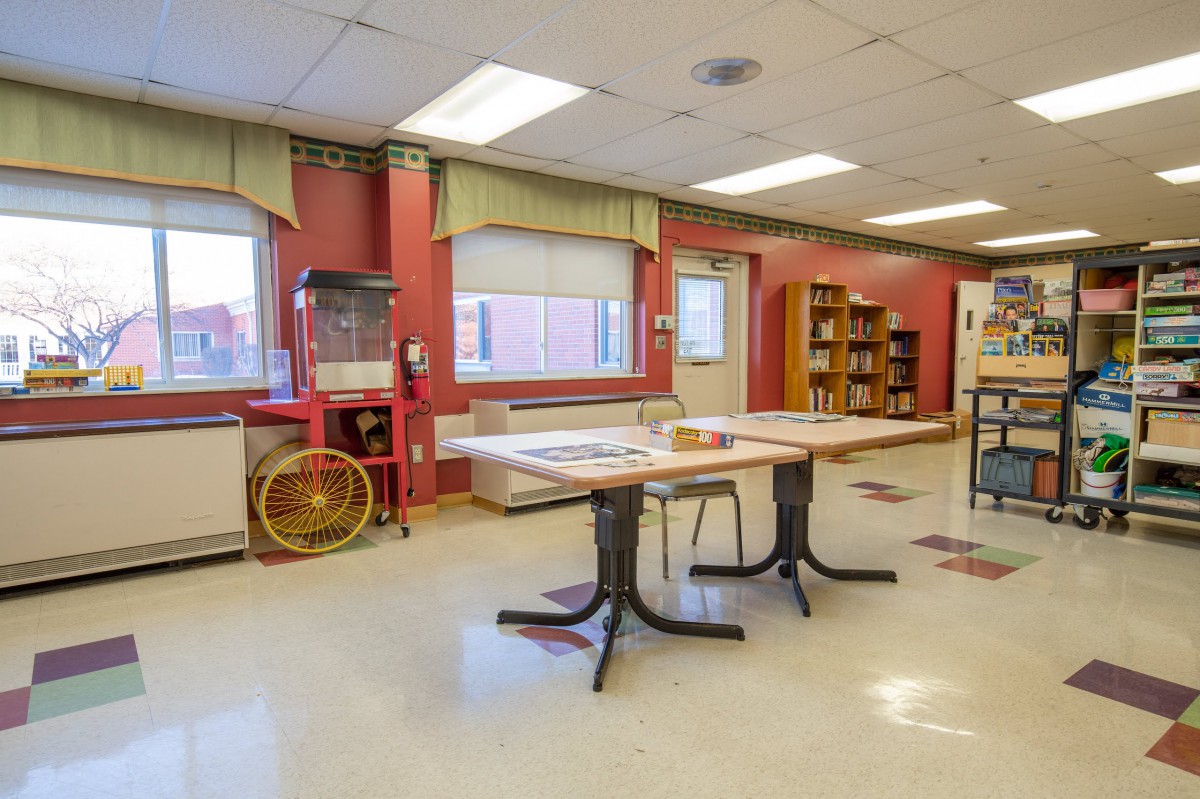 An empty classroom with tables, chairs, bookshelves, and a popcorn machine.