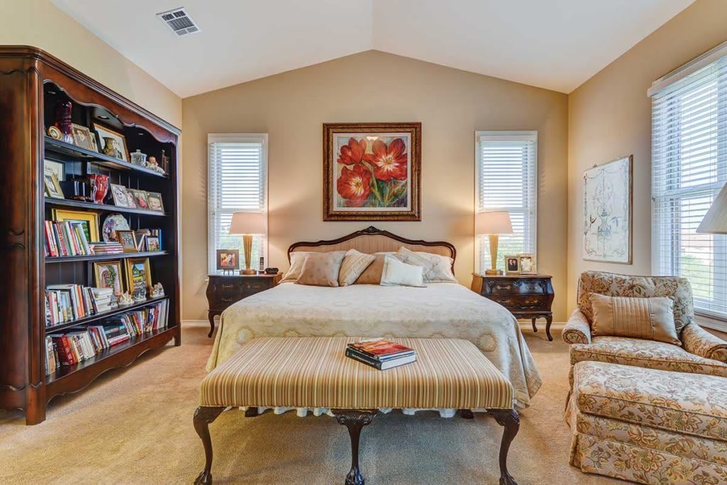 A cozy bedroom with elegant furniture, artwork above the bed, and a well-stocked bookshelf.