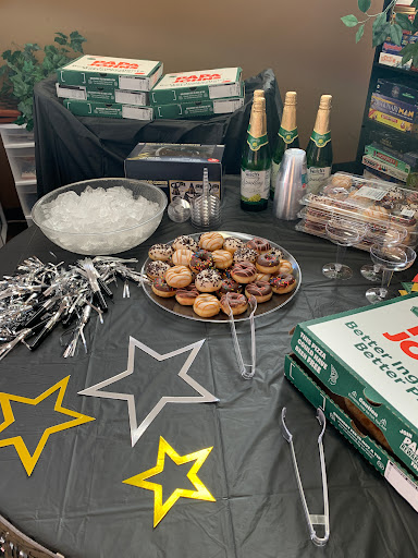 A festive party spread featuring donuts, pizza boxes, and sparkling beverages.