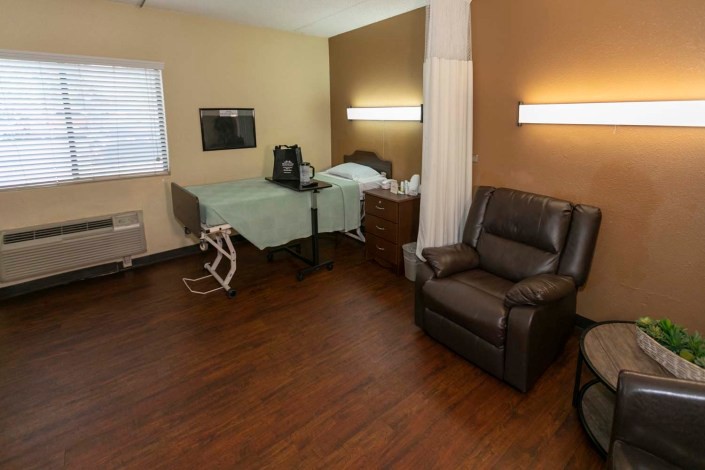 A hospital room with a bed, medical equipment, and a reclining chair on a wooden floor.