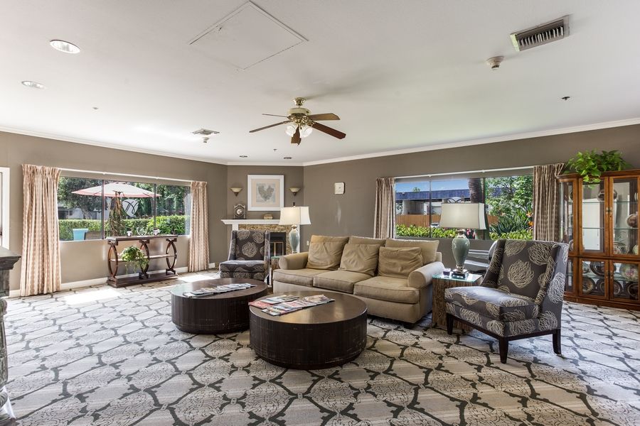 A spacious living room with comfortable seating, a ceiling fan, and large windows overlooking greenery.