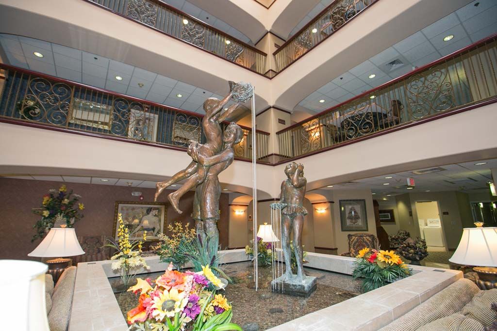 An indoor atrium featuring a dynamic sculpture with a fountain surrounded by colorful flowers.