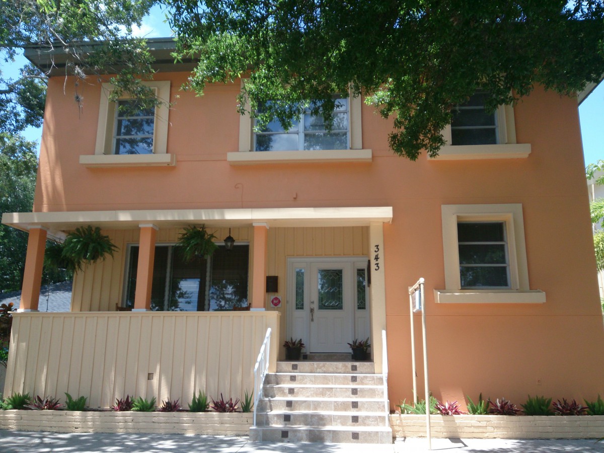 A two-story peach-colored house with a front porch and surrounding greenery.