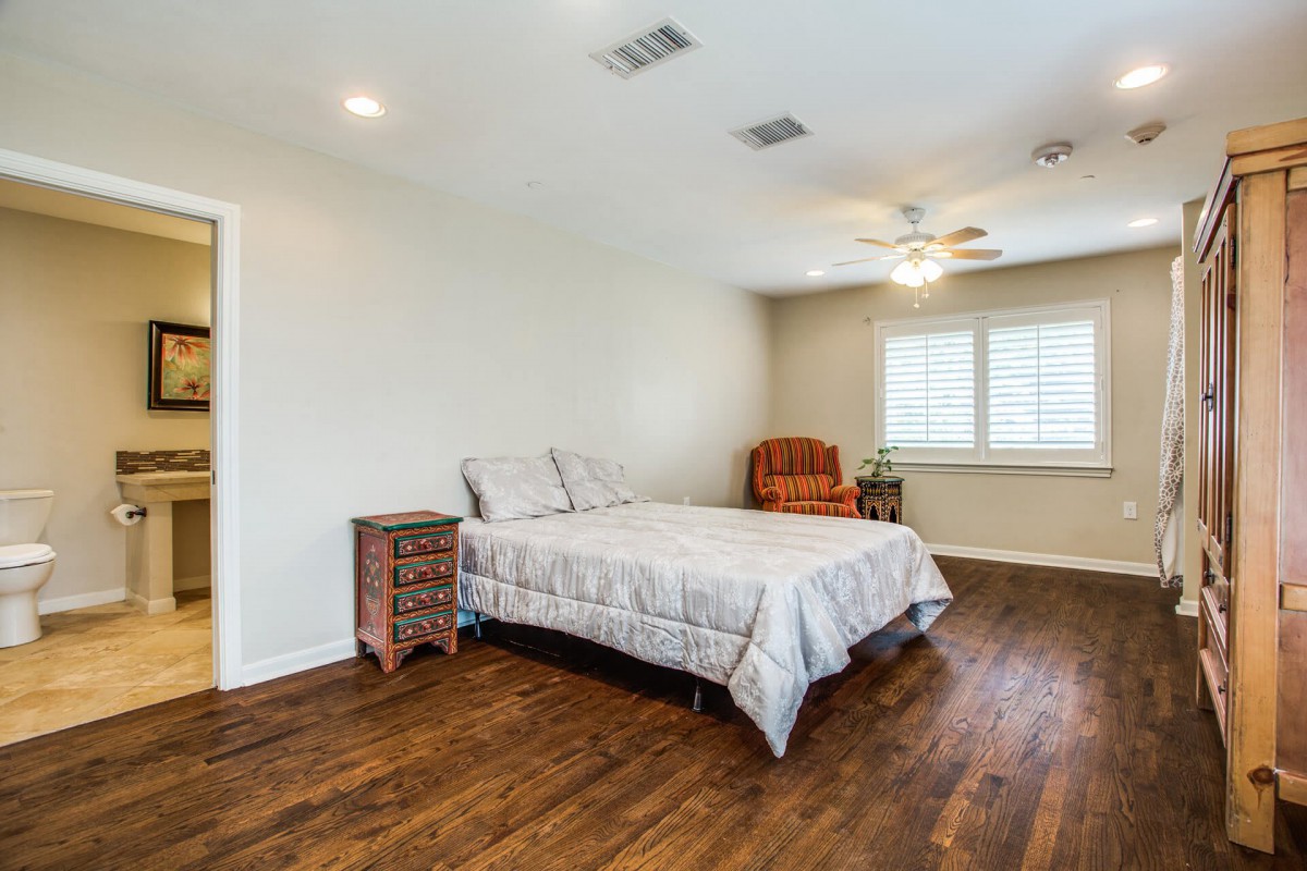 A spacious bedroom with a bed, wooden flooring, and a ceiling fan.