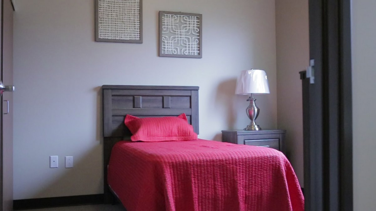 A minimalist bedroom featuring a single bed with vibrant red bedding and a modern nightstand topped with a stylish lamp.