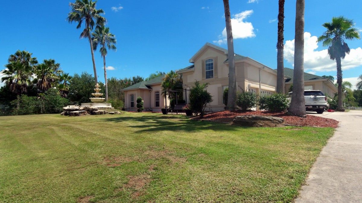A large two-story house with a fountain and palm trees in the front yard on a sunny day.