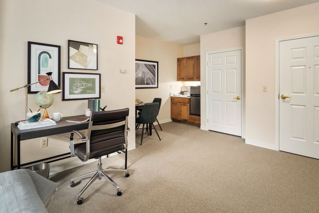 A modern office space with a desk, chair, and artwork, adjacent to a kitchenette.