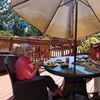 A person enjoys a meal outdoors under an umbrella on a deck.
