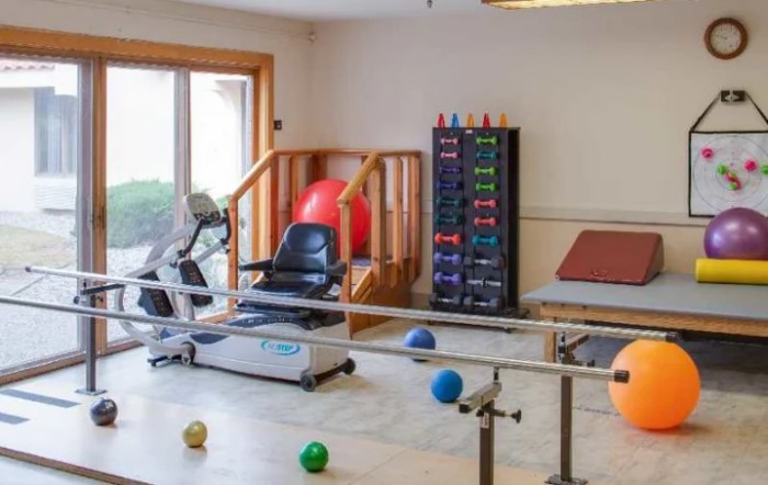 A therapy room equipped with exercise machines, fitness balls, and parallel bars for rehabilitation.