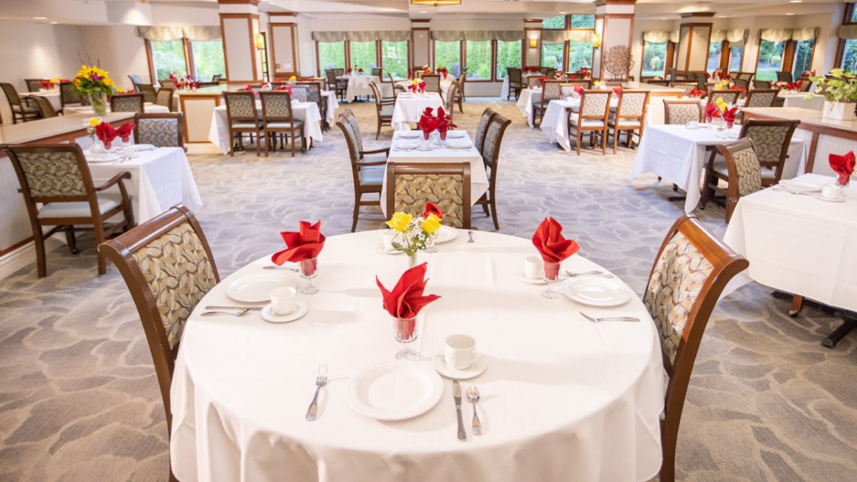 A beautifully set restaurant dining room with elegant white tablecloths and red napkin accents.