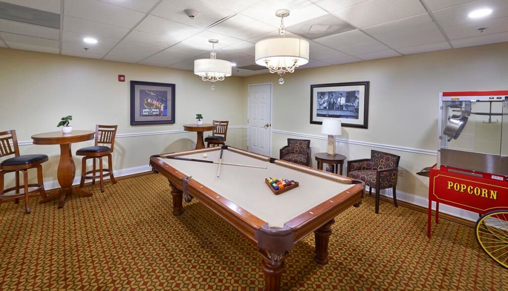 A recreation room featuring a pool table with chandeliers, artwork on the walls, and seating arrangements.