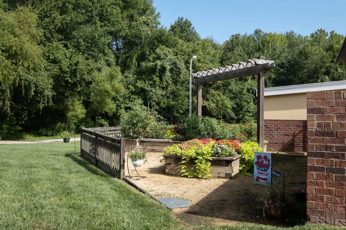 A serene garden with a pergola and lush greenery under a clear blue sky.