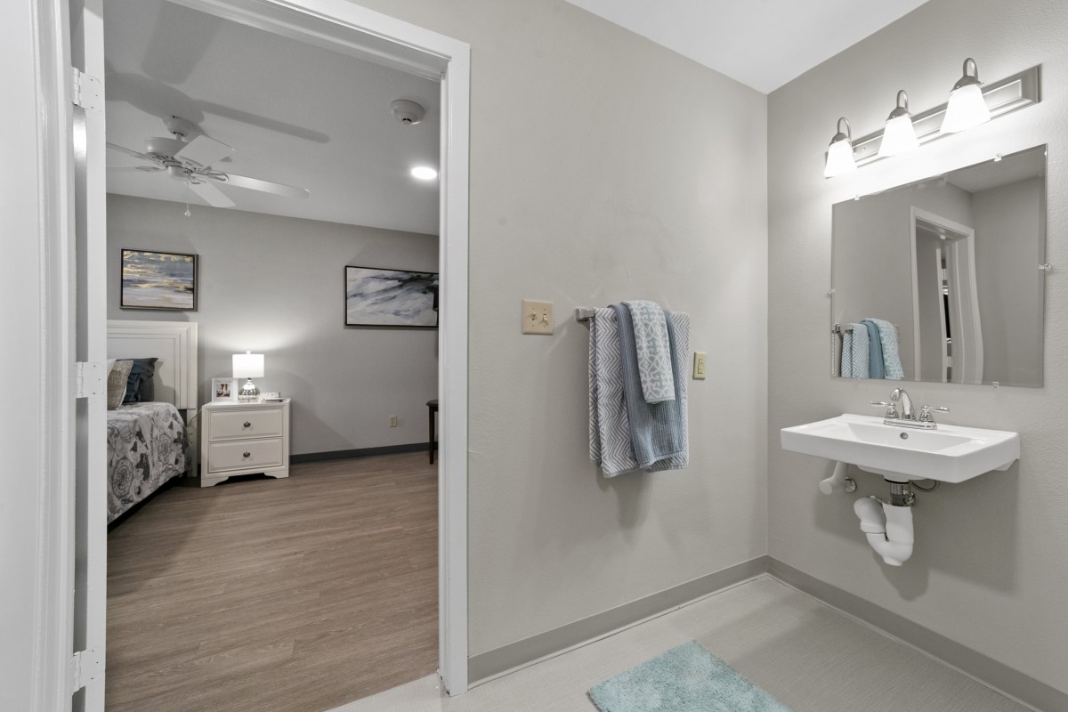 A modern bathroom with a view into a neatly decorated bedroom, showcasing neutral tones and contemporary design.