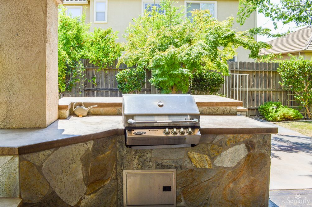 An outdoor built-in grill setup in a sunny backyard patio.
