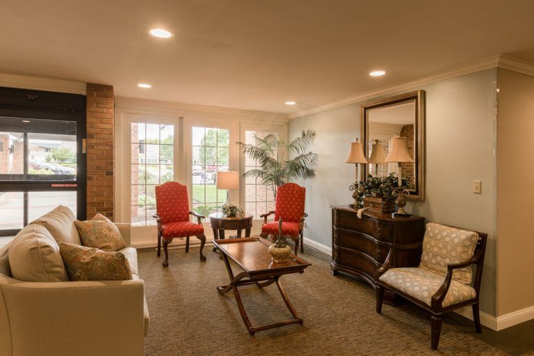 A cozy and traditional living room with warm lighting, featuring red chairs, a sofa, a wooden coffee table, lamps, and an indoor plant.