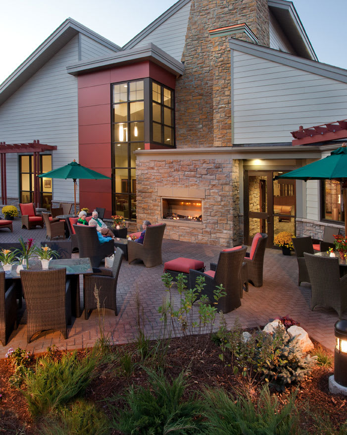 A cozy outdoor restaurant patio with a fireplace and umbrella-covered tables.