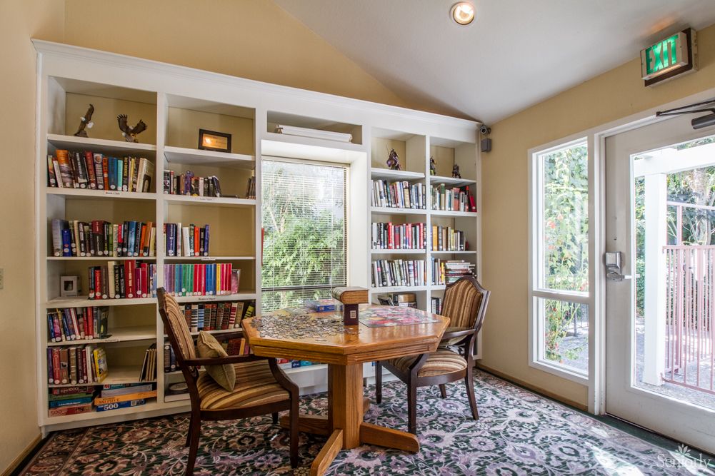 A cozy reading room with bookshelves, a round table, and chairs by the window.