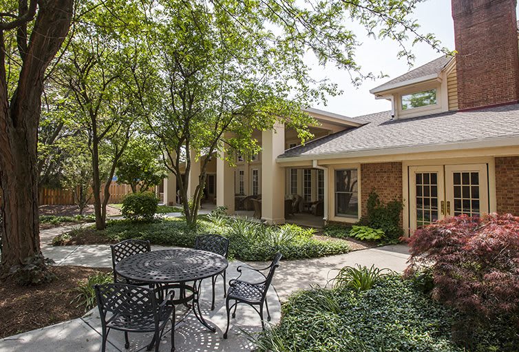 A serene outdoor patio area with a table, chairs, and lush greenery surrounding a building.