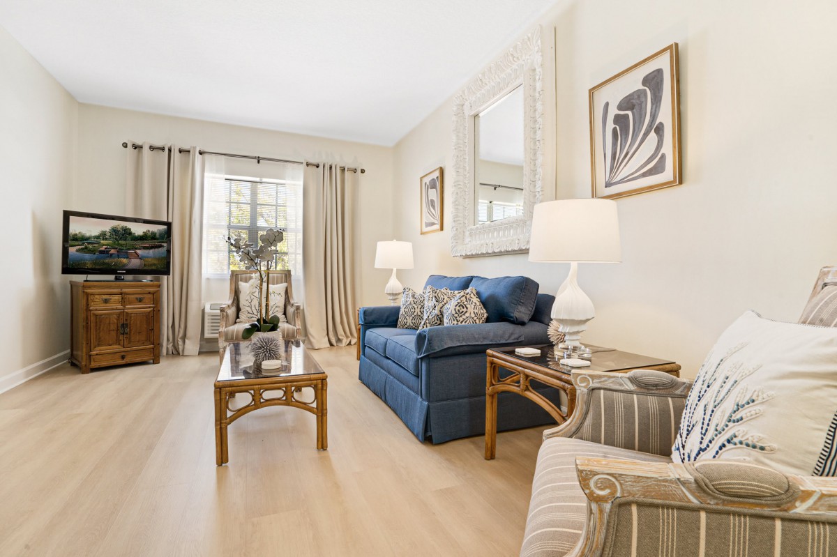 A cozy living room with a blue sofa, wooden coffee table, and elegant decor, featuring artwork on the walls and a TV in the corner.