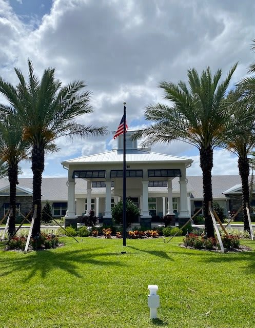 A symmetrical view of a building with palm trees and an American flag in front, set against a cloudy sky.