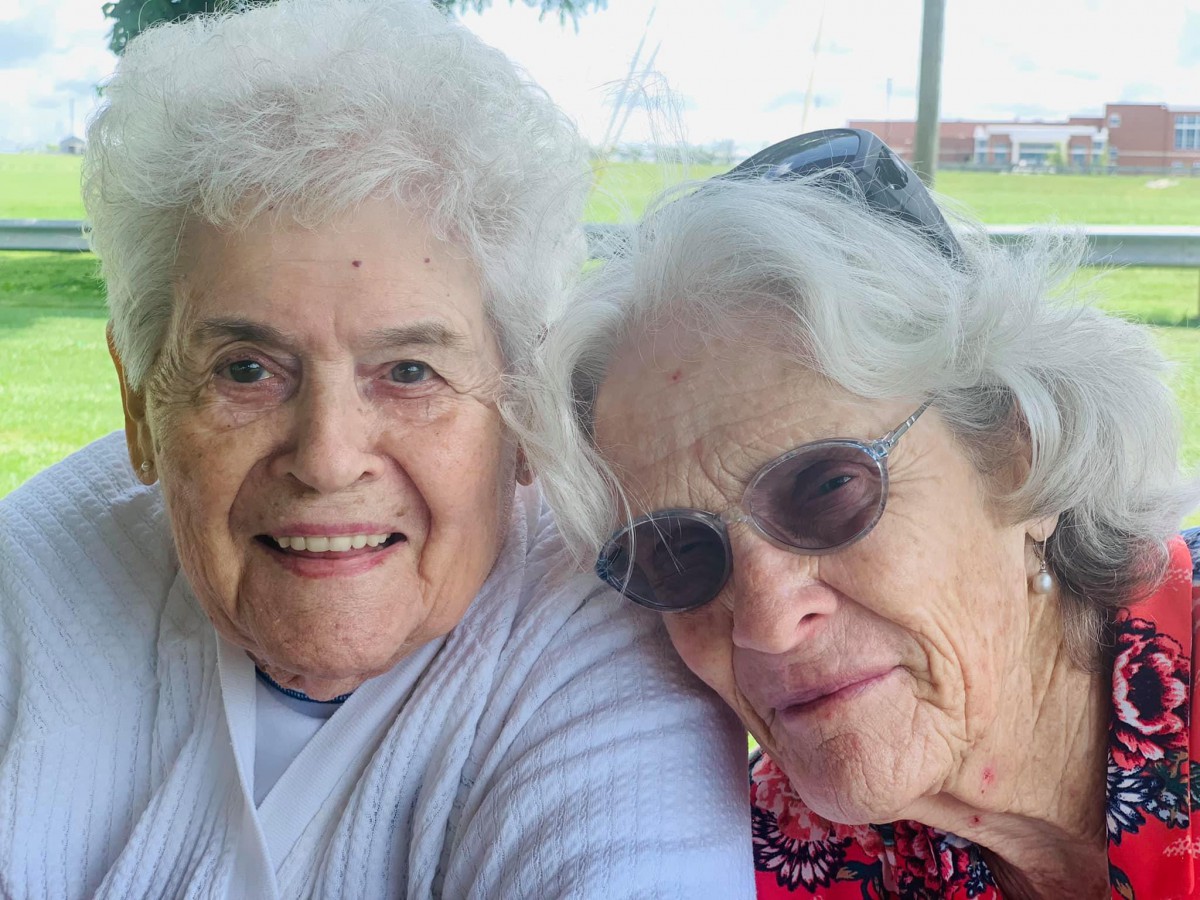 Two elderly women smiling and enjoying each other's company outdoors.