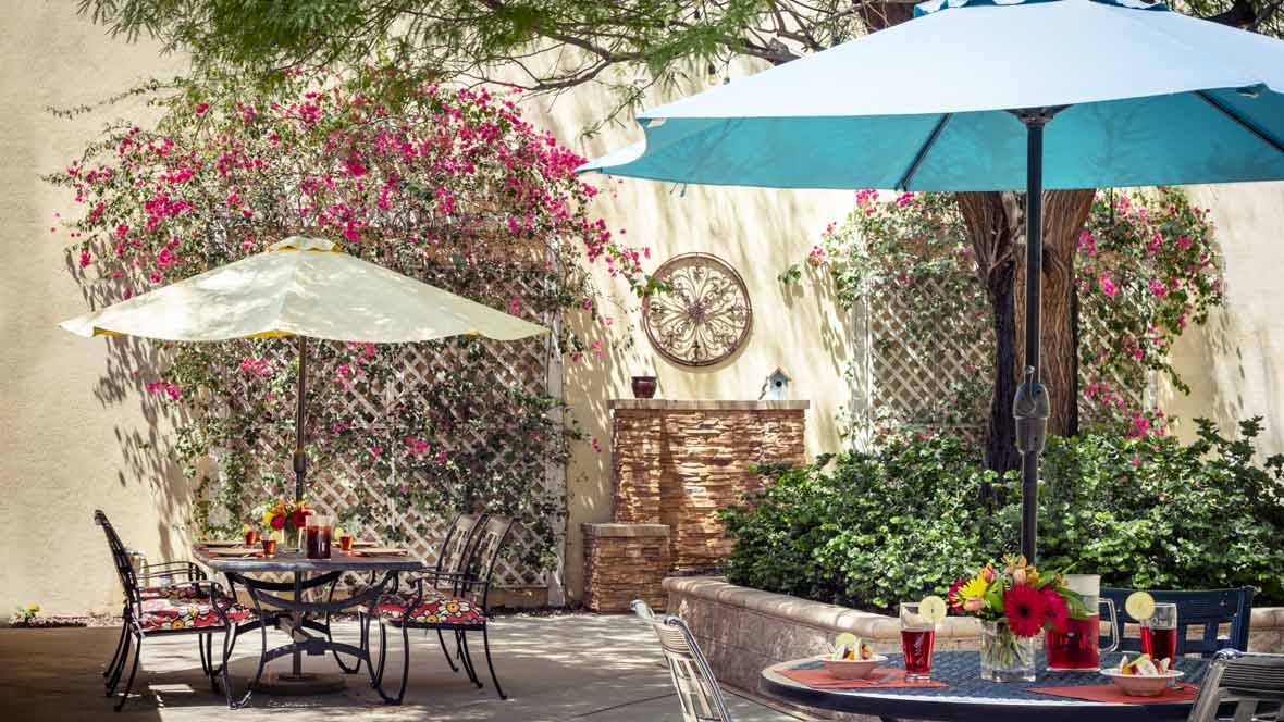 A charming outdoor patio area with tables and umbrellas, surrounded by lush plants and colorful flowers.