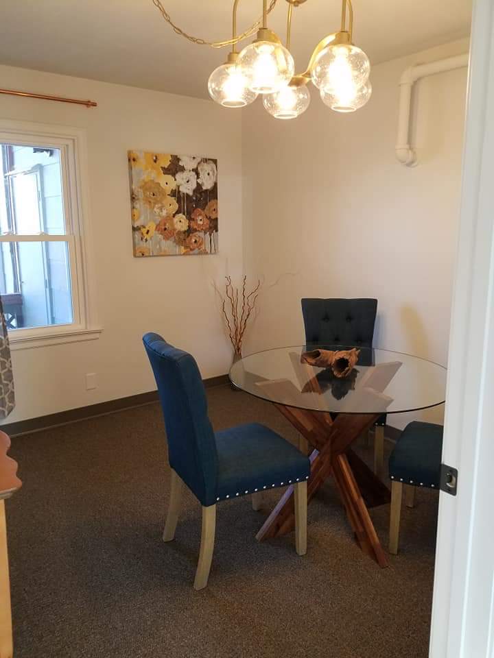 A modern dining room with a glass table and blue upholstered chairs, featuring wall art and a window.