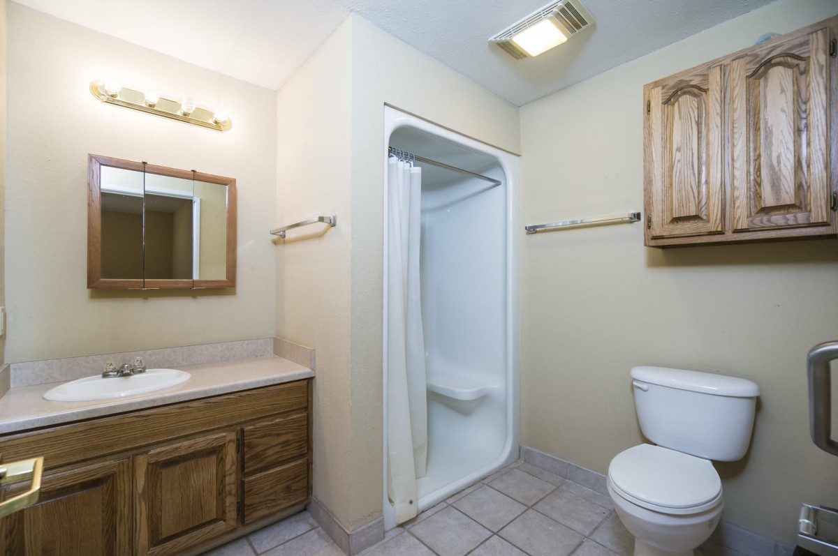 A clean and simple bathroom with a shower, toilet, and wooden vanity.