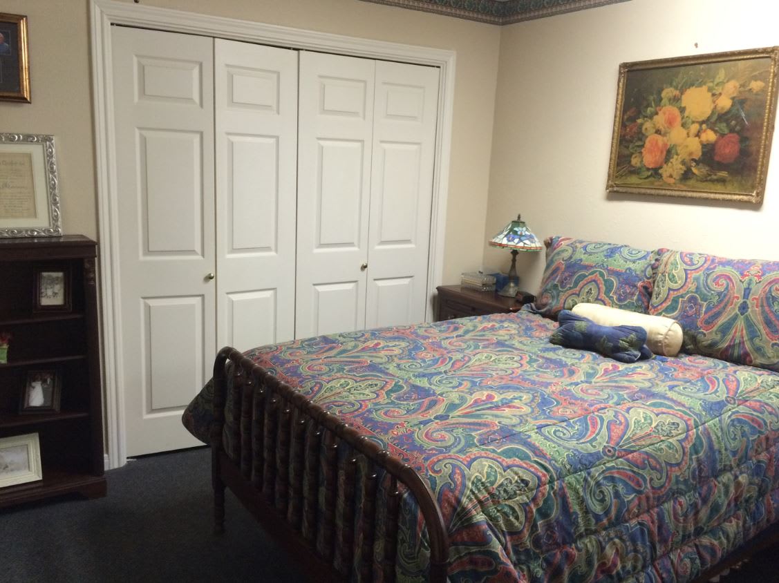 A cozy bedroom featuring a bed with colorful bedding, a nightstand with a lamp, and a closed closet door.