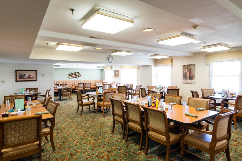 A well-lit dining room with several tables and chairs, featuring a carpeted floor.