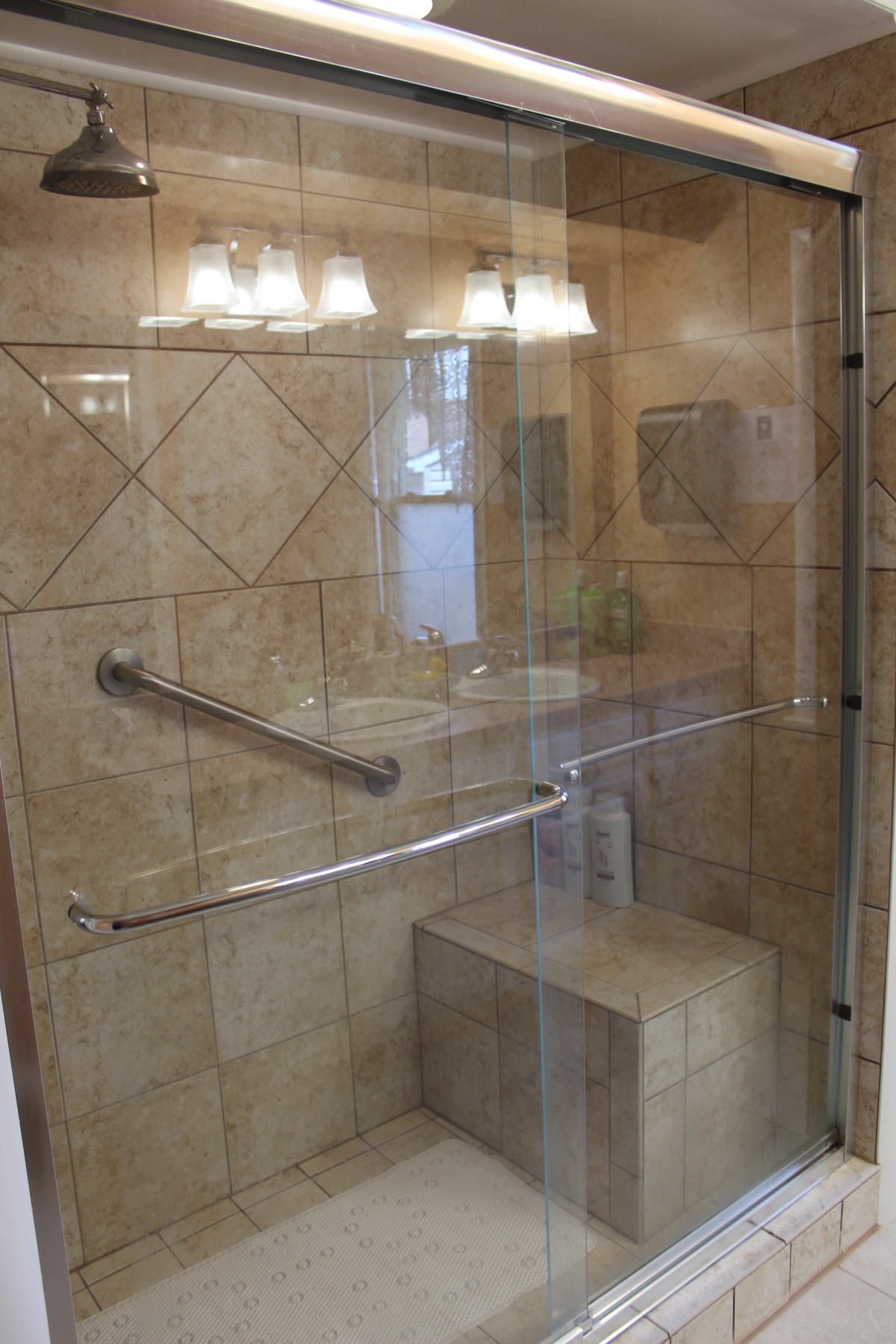 Modern shower with glass door, tiled walls, seating, and grab bars.