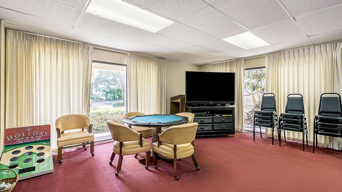 A cozy living room with a TV, round table, and chairs by large windows.