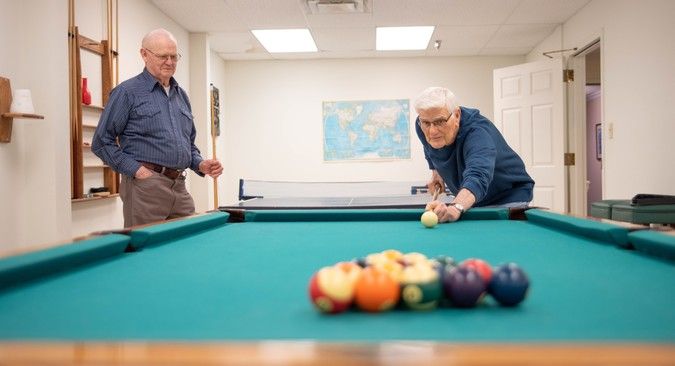 Two people engaged in a game of billiards in a recreation room.