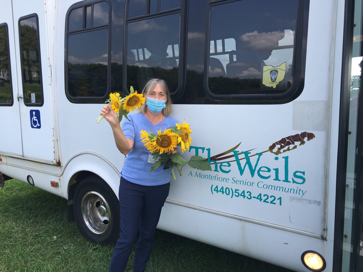 Person holding sunflowers while standing beside a bus.