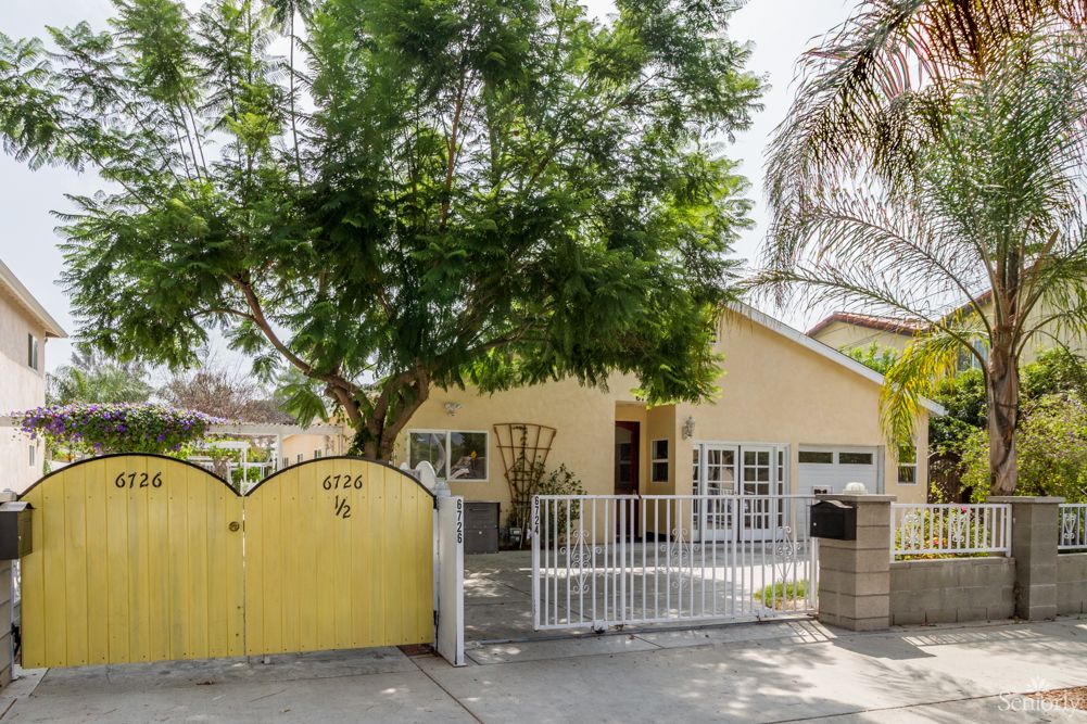 A charming house with a yellow gate and lush trees in the front yard.