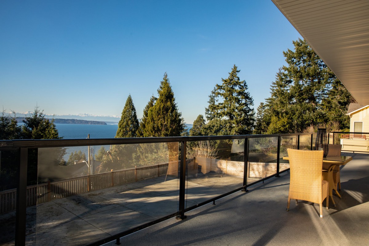 A scenic view from a balcony overlooking trees and a distant coastline under a clear blue sky.