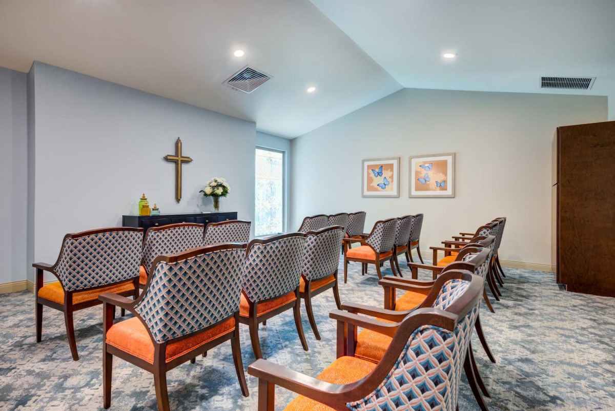 A small chapel with rows of chairs and a cross on the wall.