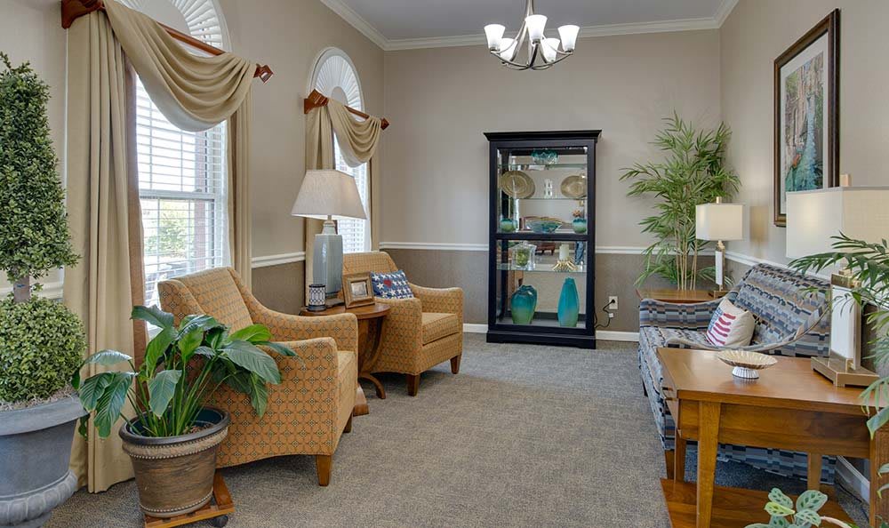A cozy living room with wicker chairs, decorative plants, and a glass cabinet.