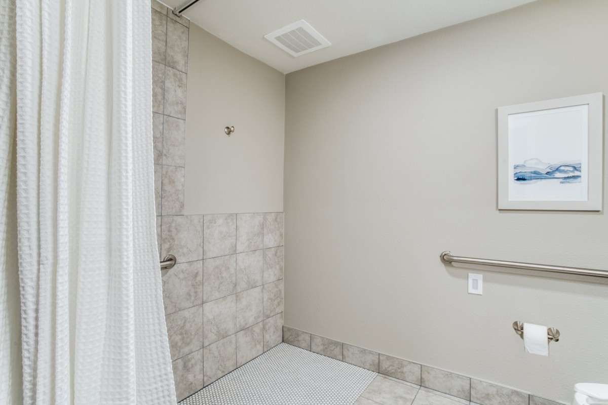 A minimalist bathroom featuring a tiled shower area and a grab bar.